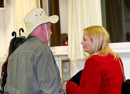 Ein Mann und eine Frau stehen sich gegenüber. Der Mann trägt einen Hut und die Frau trägt einen roten Mantel. Sie führen wahrscheinlich ein Gespräch.