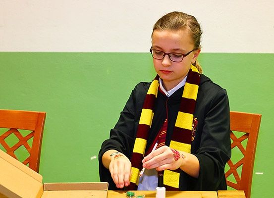Ein junges Mädchen in einem Hogwarts-Schal sitzt an einem Schreibtisch und malt mit einem Pinsel.