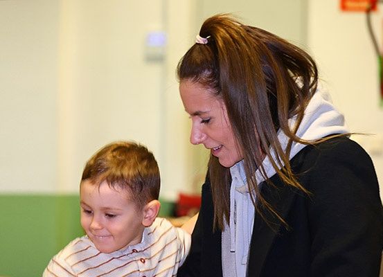 Eine Frau mit braunen Haaren lächelt, während sie neben einem Jungen steht. Der Junge trägt ein gestreiftes Shirt und schaut die Frau an.