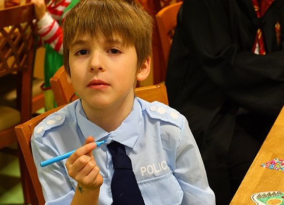 Ein junger Junge in einer Polizeiuniform sitzt an einem Tisch, hält einen blauen Stift und schaut nach unten.