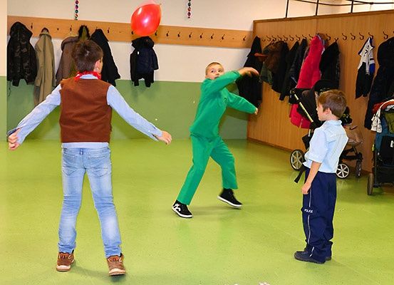 Drei Jungen spielen drinnen mit einem roten Ballon. Ein Junge versucht ihn zu fangen, während die anderen zusehen.
