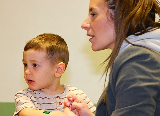 Ein junger Junge mit einem gestreiften Shirt schaut neugierig eine erwachsene Frau an, die seine Hand hält und ihm scheinbar etwas sagt.
