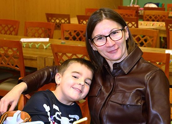 Eine Frau und ein junger Junge sitzen lächelnd zusammen an einem Tisch, in einem Raum mit um sie herum angeordneten Stühlen und Tischen.