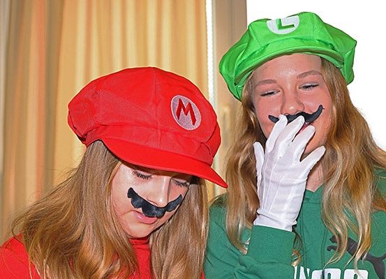 Zwei Frauen in Mario- und Luigi-Kostümen mit Schnurrbart und grüner Mütze scheinen für ein Foto zu posieren.