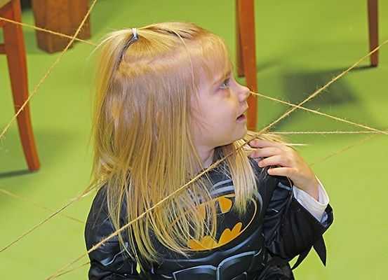 Ein kleines Mädchen mit blonden Haaren, das einen Batman-Kostüm trägt und ein Seil hält.
