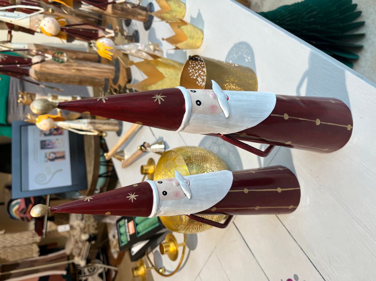 Zwei rote und weiße Weihnachtsmannfiguren mit goldenen Akzenten und Sternmustern sind auf einem weißen Tisch ausgestellt, zusammen mit verschiedenen anderen Ornamenten und Gegenständen.