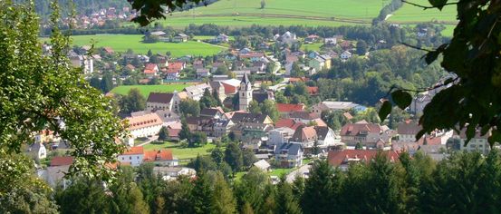 Ein malerisches Dorf in einem Tal, umgeben von üppigen grünen Feldern und bewaldeten Bergen.
