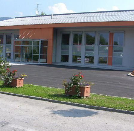 Ein modernes Gebäude mit einem Metalldach und großen Fenstern, zwei Blumentöpfen und einer Einfahrt davor.