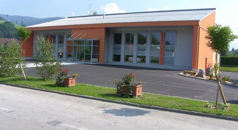Ein modernes Gebäude mit einem Metalldach und großen Fenstern, zwei Blumentöpfen und einer Einfahrt davor.