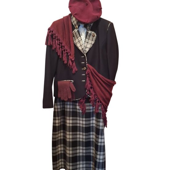 Ein burgunderroter Hut, eine schwarze Jacke mit rotem Schal, eine karierte Weste, ein roter Handschuh und ein karierter Rock.