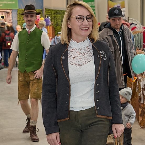 Eine Frau in grünen Hosen und einem Cardigan geht an einem Mann in traditionellen Lederhosen und einem jungen Jungen mit Hut vorbei.