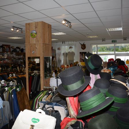 Ein Bekleidungsgeschäft mit vielen Hüten zur Schau, darunter schwarze und grüne. Es gibt Kleidung an Kleiderstangen und Regalen, und ein Hirschkopf ist an der Wand montiert.