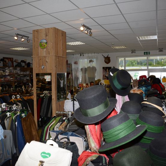 Ein Bekleidungsgeschäft mit vielen Hüten zur Schau, darunter schwarze und grüne. Es gibt Kleidung an Kleiderstangen und Regalen, und ein Hirschkopf ist an der Wand montiert.