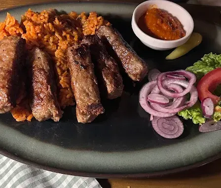 Ein Teller mit gegrillten Würstchen, Reis, Zwiebeln und Salat auf einem Holztisch.