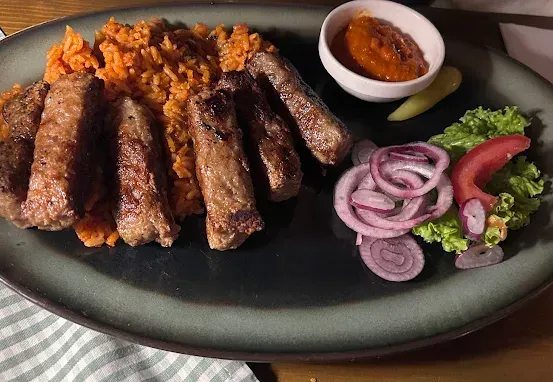 Ein Teller mit gegrillten Würstchen, Reis, Zwiebeln und Salat auf einem Holztisch.