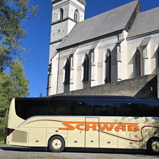 Ein Bus mit dem Wort Schwab darauf parkt vor einer Kirche mit aufwendigen Verzierungen an ihren Wänden.