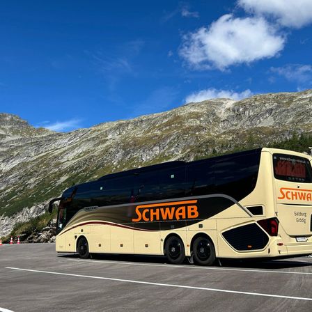 Ein Doppeldecker-Bus mit dem Wort 'Schwab' an der Seite, geparkt vor einem Berg unter blauem Himmel.
