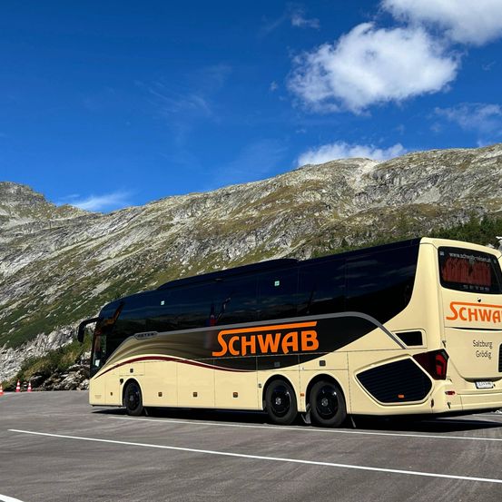 Ein Doppeldecker-Bus mit dem Wort 'Schwab' an der Seite, geparkt vor einem Berg unter blauem Himmel.