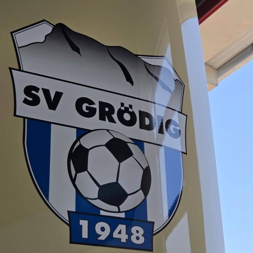 Ein Logo für den Fußballverein SV Grödig, das einen Fußball mit dem Jahr 1948 darunter zeigt. Das Logo ist auf einem blau-weiß gestreiften Hintergrund platziert.