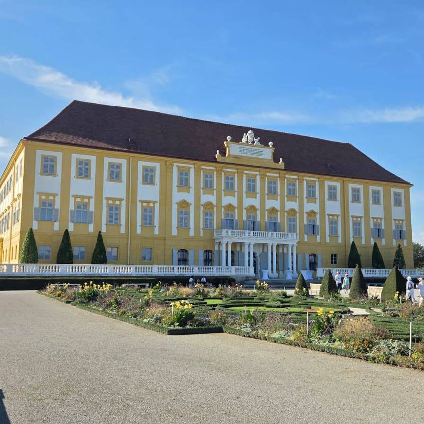 Ein großes gelbes Gebäude mit einem braunen Dach und vielen Fenstern steht inmitten eines gut gepflegten Gartens.