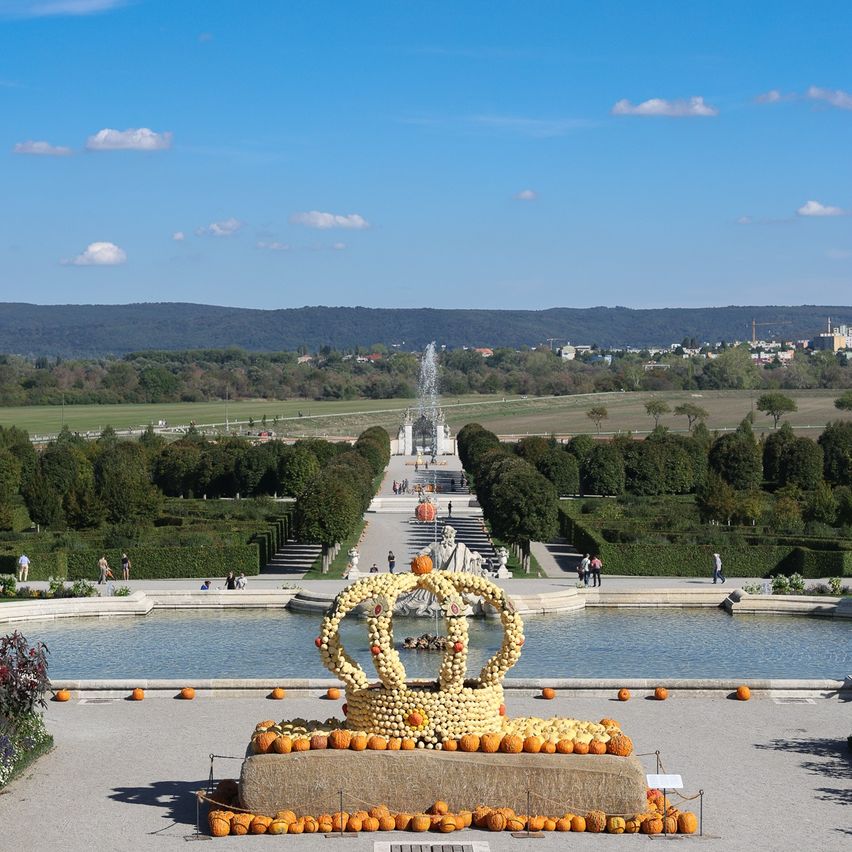 Eine Kürbiskronen wird vor einem Brunnen in einem Garten ausgestellt.