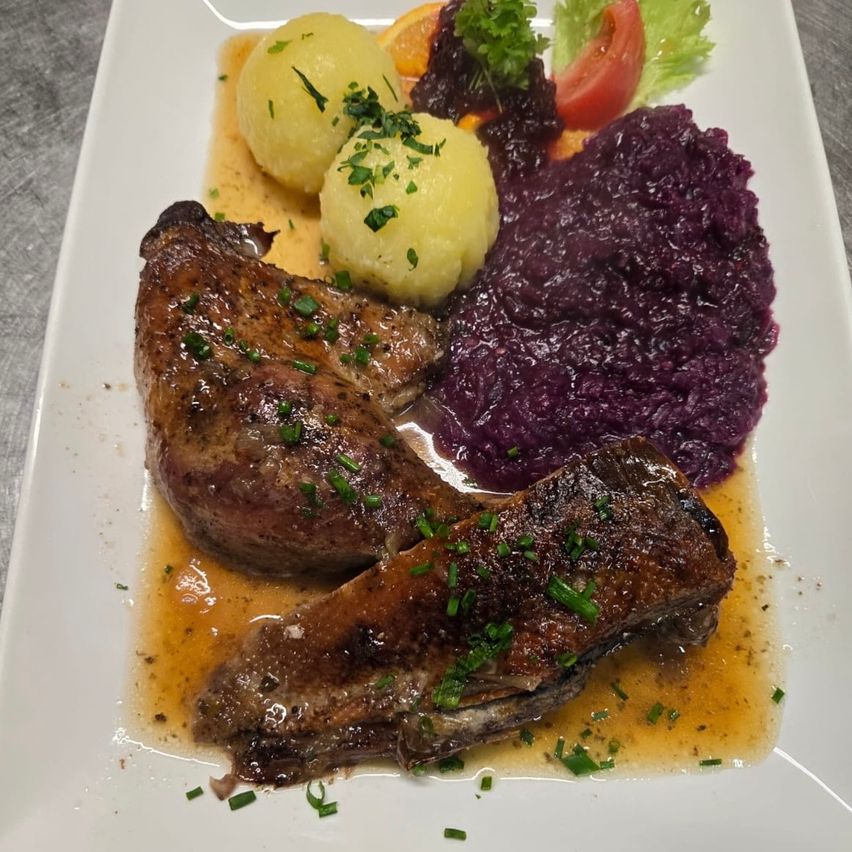 Ein Teller mit zwei gegrillten Fleischstücken, übergossen mit Sauce, begleitet von Kartoffelpüree und Rotkohl.