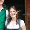 Ein Mann und eine Frau stehen eng beieinander und lächeln für ein Foto. Der Mann trägt eine grüne Weste und braune Hose. Die Frau ist in einem traditionellen grünen Kleid gekleidet. Sie scheinen auf einem Festival oder einer Feier zu sein.