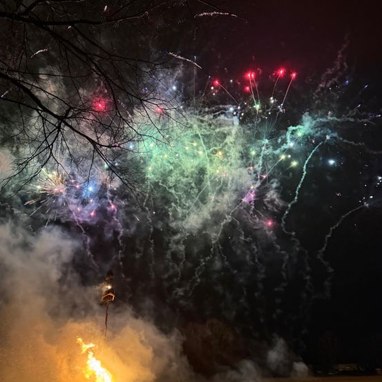 Ein lebhafter Nachthimmel, gefüllt mit Feuerwerken in verschiedenen Farben wie Rot, Grün und Lila. Die Feuerwerke explodieren und erzeugen eine wunderschöne Darstellung am dunklen Himmel.