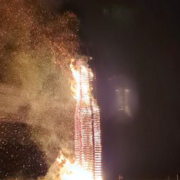 Ein hoher Holzbau brennt nachts hell, Flammen und Funken erhellen den dunklen Himmel.