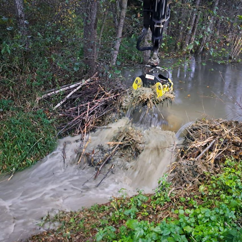 Ein großer mechanischer Arm entnimmt schmutziges Wasser aus einem Flussbett und lagert Ablagerungen in einem Haufen am Ufer ab.