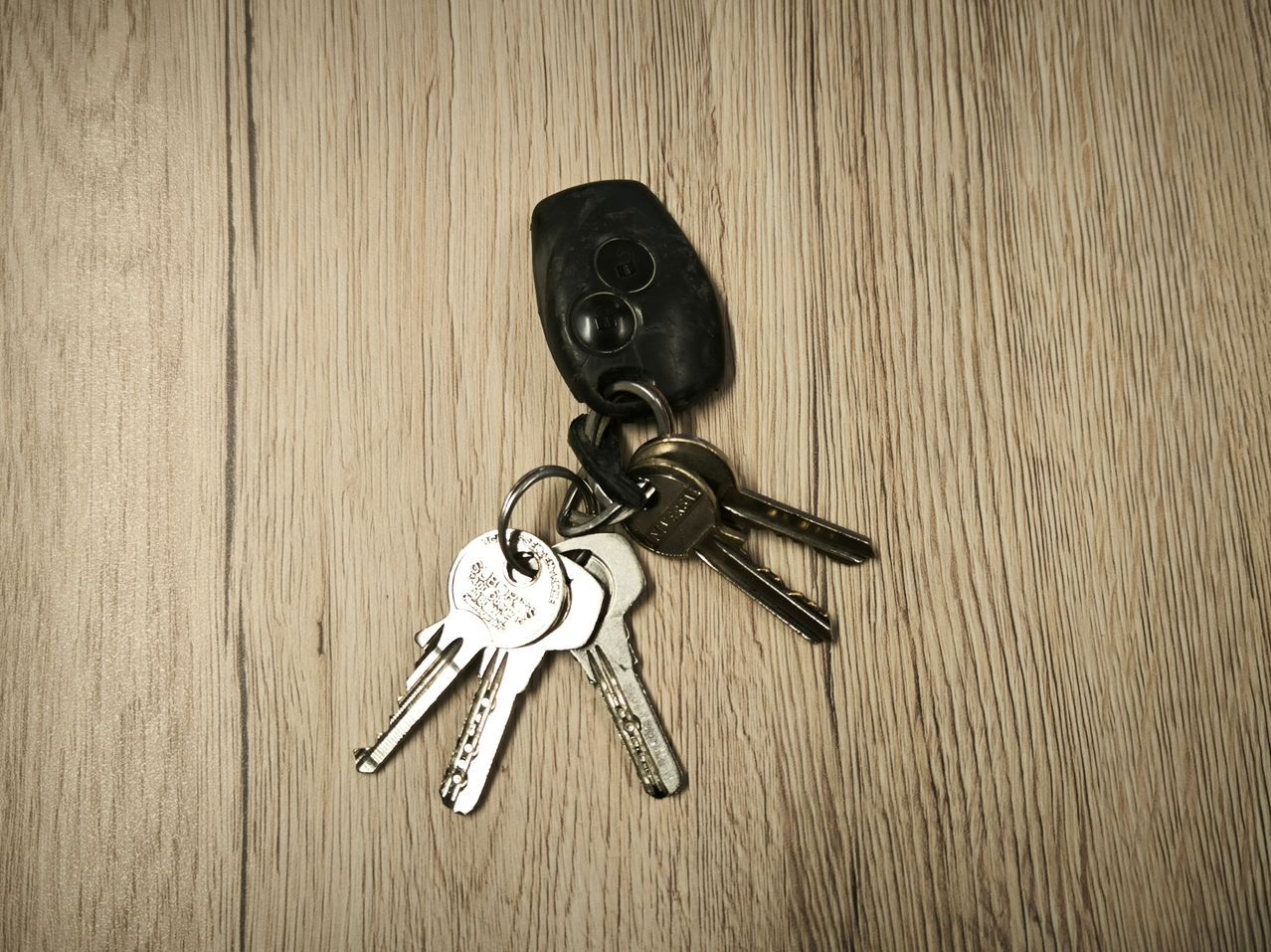 Mehrere silberne Schlüssel und ein schwarzer Fernbedienungsschlüssel liegen auf einer Holzoberfläche. Der Fernbedienungsschlüssel hat oben einen runden Knopf.