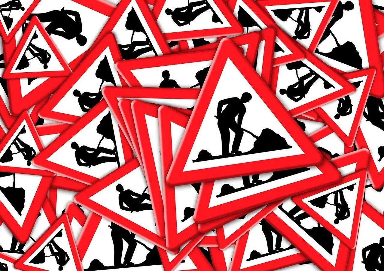 Eine Sammlung roter und weißer dreieckiger Verkehrszeichen mit Silhouetten von Bauarbeitern, wobei jedes Schild einen Arbeiter in verschiedenen Posen auf einer Baustelle zeigt.