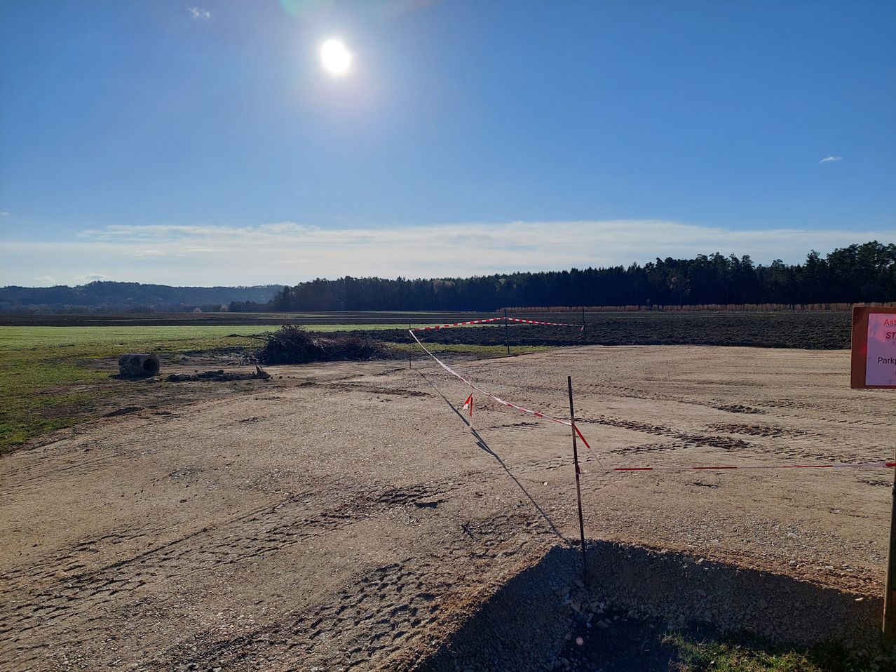 Ein sonniger Tag über einem offenen Feld mit einem Erdweg, einem kleinen Loch und roten und weißen Barrikaden. In der Ferne stehen Bäume.