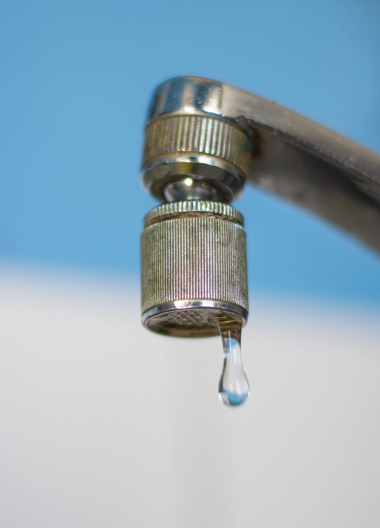 Ein Nahaufnahme eines Wasserhahns mit einem einzelnen Wassertropfen, der gegen einen blauen Hintergrund fällt.