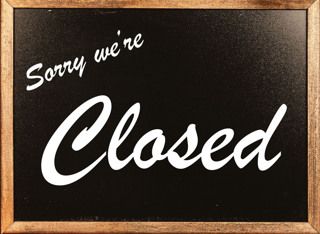Ein schwarzes Brett mit weißem Text, der 'Sorry we're Closed' lautet. Der Text ist in kursiver Schrift geschrieben und zentriert auf dem Brett. Das Brett hat einen Holzrahmen.