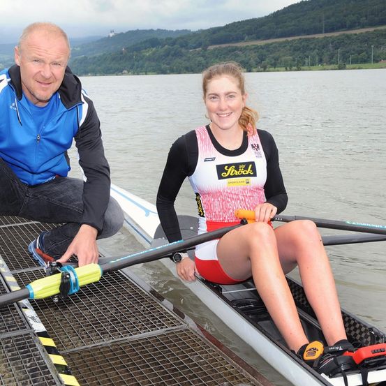 Ein Mann und eine Frau sind in einem Boot auf einem Fluss. Der Mann lächelt und schaut die Frau an, die ein Paddel hält.
