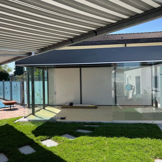 Ein moderner Patiobereich mit Glaswänden und versenkbarem Dach befindet sich neben einem Rasen und einem Pool.