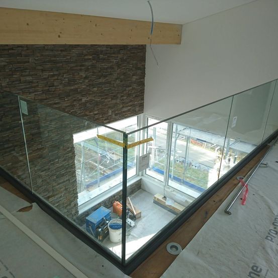 Ein Baustelle mit einer Glasbrüstung, die auf eine Straße blickt. Es sind Materialien und Werkzeuge verstreut. Die Wand dahinter ist aus Stein.