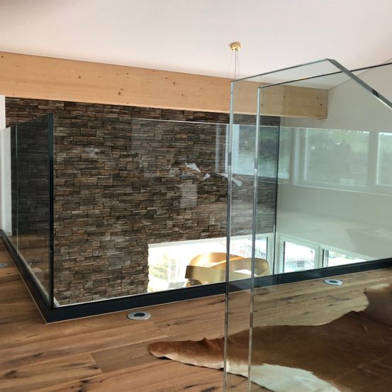 Ein modernes Interieur mit einer Glaswand und einer Ziegelwand. Der Boden ist aus Holz und es liegt ein Fellteppich auf dem Boden.