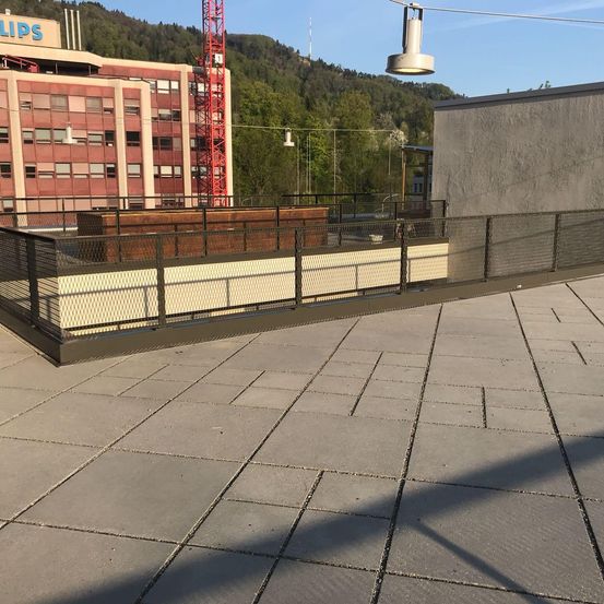 Ein Dachbereich mit gefliestem Boden und Metallgeländern. Ein großes Gebäude und ein Kran sind im Hintergrund zu sehen.