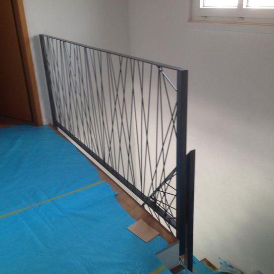 Ein Metallgeländer steht auf einem blauen Boden. Es hat ein geometrisches Muster und lehnt sich an eine weiße Wand.