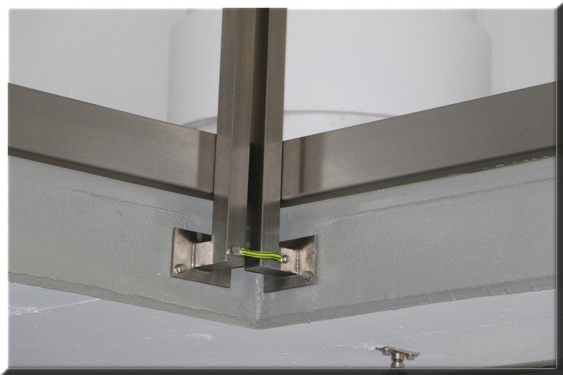 A close-up view of a metal ceiling fixture with a square shape, featuring a white glass cover and a green wire connected to the metal brackets.