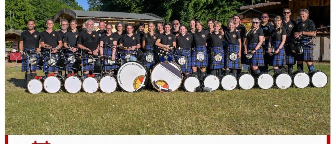 Eine Gruppe von Dudelsackspielern und Trommlern in Kilts, die für ein Foto auf einem Rasenfeld mit einem roten Banner mit der Aufschrift 'Oberpullendorfer Kulturtage' posiert.