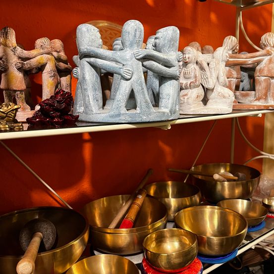 Eine Ausstellung von tibetischen Klangschalen, Figuren und anderen spirituellen Artefakten auf einem Regal an einer orangefarbenen Wand.