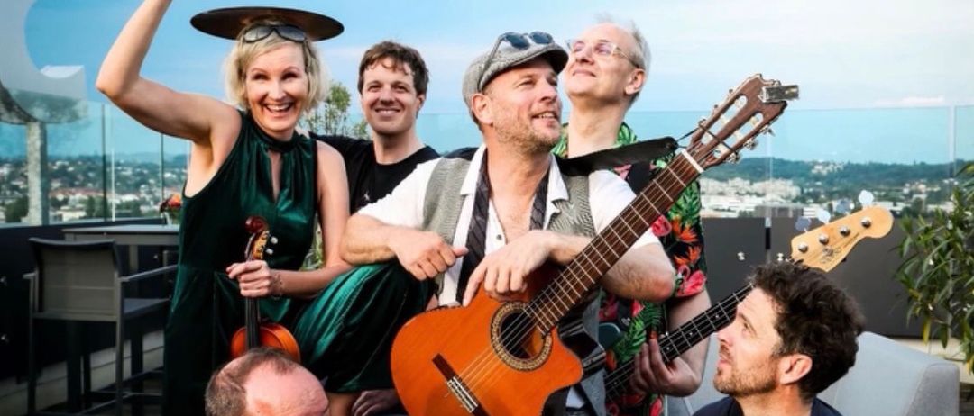 Fünf Personen posieren mit Musikinstrumenten auf einem Dach. Eine Frau hält eine Geige und ein Mann spielt Gitarre. Der Mann in der Mitte trägt einen Hut. Der Text lautet, Live am Lendwirbel Scherbe Graz, Fr, 1. Mai, 17:30.