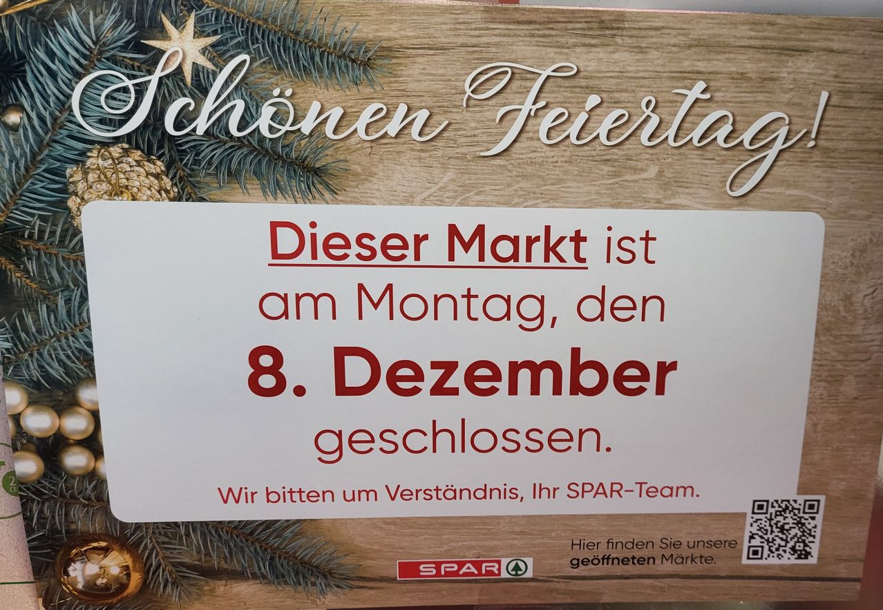 Schild auf einem hölzernen Hintergrund mit einer Weihnachtsbaum-Dekoration. Es steht geschrieben: 'Dieser Markt ist am Montag, den 8. Dezember geschlossen. Wir bitten um Ihr Verständnis, Ihr SPAR-Team.' Unten gibt es einen Link zu anderen geöffneten Märkten.