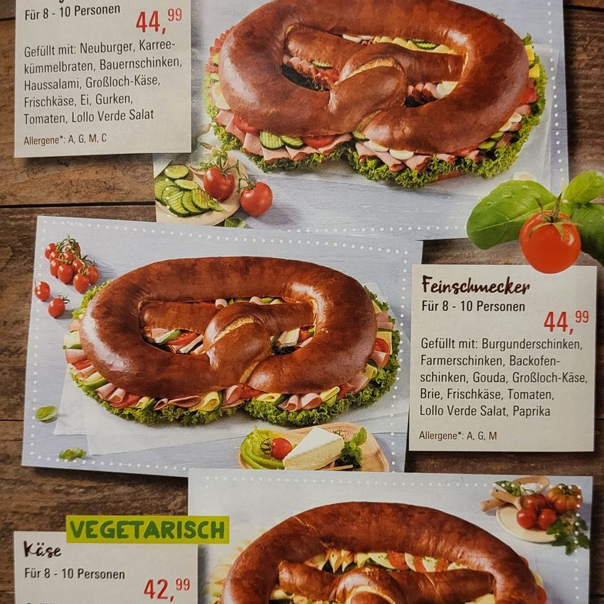 Ein Flyer zeigt drei verschiedene Sandwichplatten. Die erste zeigt ein brezelförmiges Sandwich mit verschiedenen Fleischsorten, Eiern und Gemüse, zum Preis von 44,99 für 8-10 Personen. Die zweite ist ein vegetarisches Brezelsandwich, zum Preis von 42,99 für 8-10 Personen. Die dritte, mit Feinschmecker beschriftet, enthält Fleisch, Käse und Gemüse, zum Preis von 44,99 für 8-10 Personen.