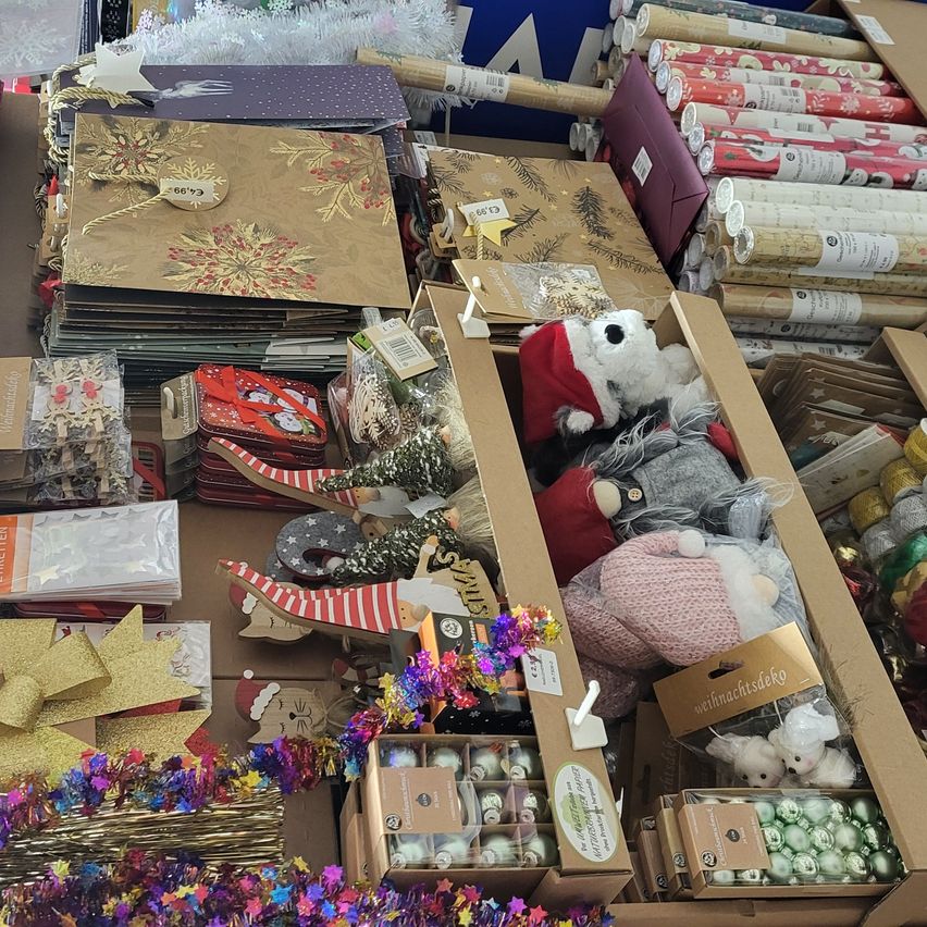 Verschiedene Weihnachtsartikel ausgestellt, darunter Geschenktüten, Geschenkpapier, Bänder, Ornamente und Plüschtiere in festlicher Umgebung. Viele Artikel zeigen den Weihnachtsmann und Weihnachtsbäume.