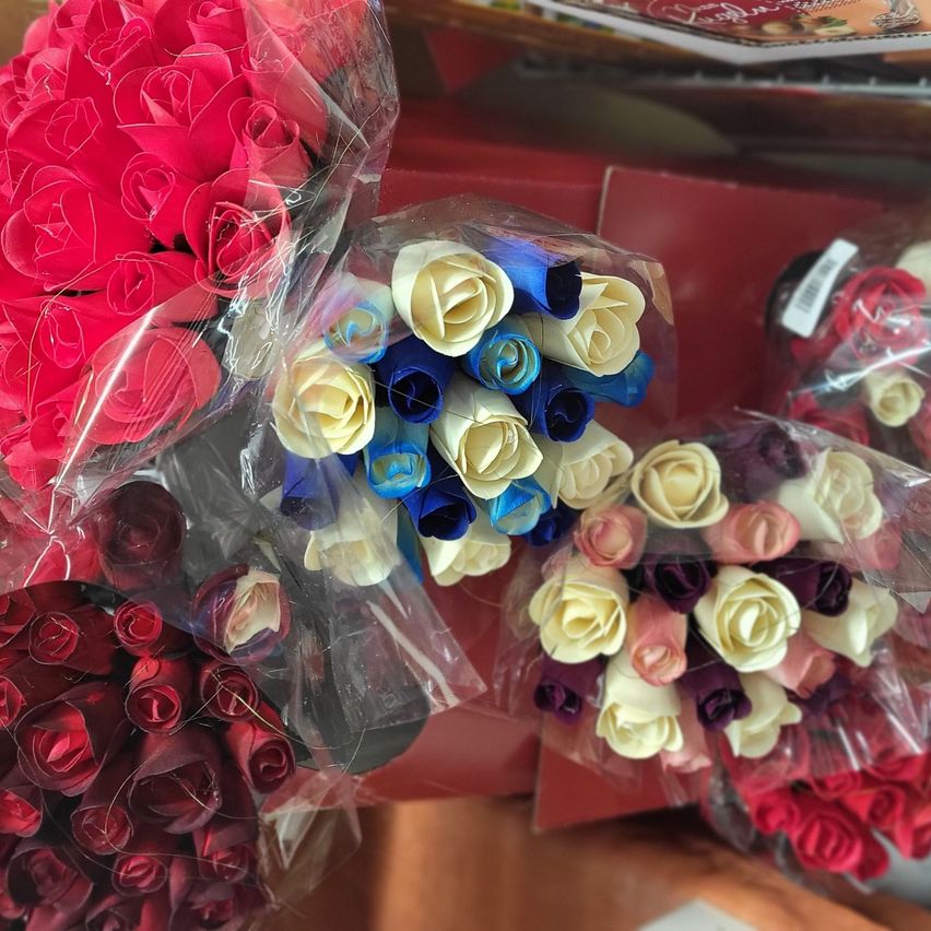 Mehrere Sträuße künstlicher Rosen in Rot, Weiß, Blau und Lila sind in Plastik verpackt. Jeder Strauß ist einzeln eingewickelt.