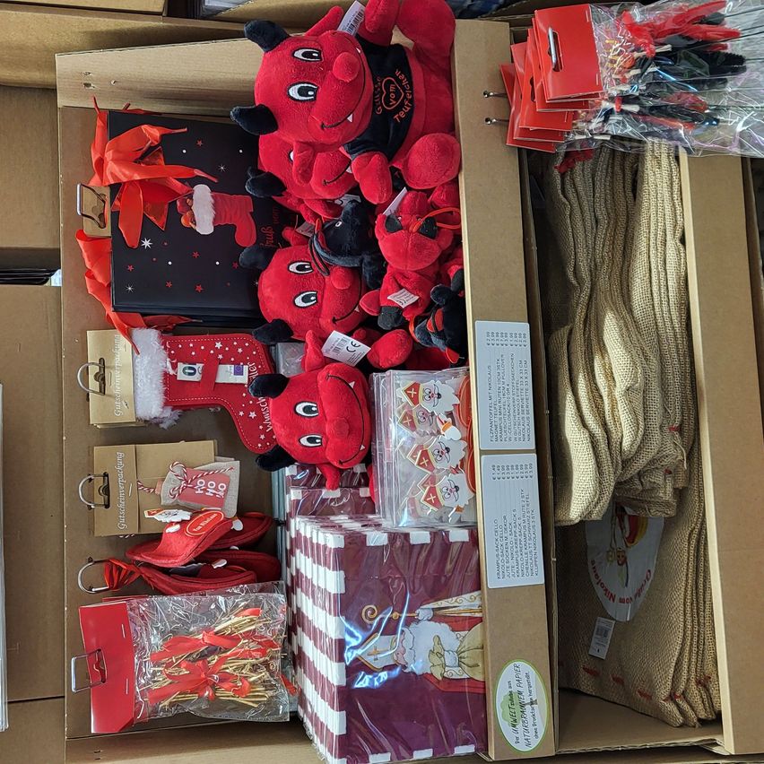 A storage box full of Christmas decorations, including red plush toys, wrapped gifts, knitted items, and festive paper. The box is open, revealing its contents.